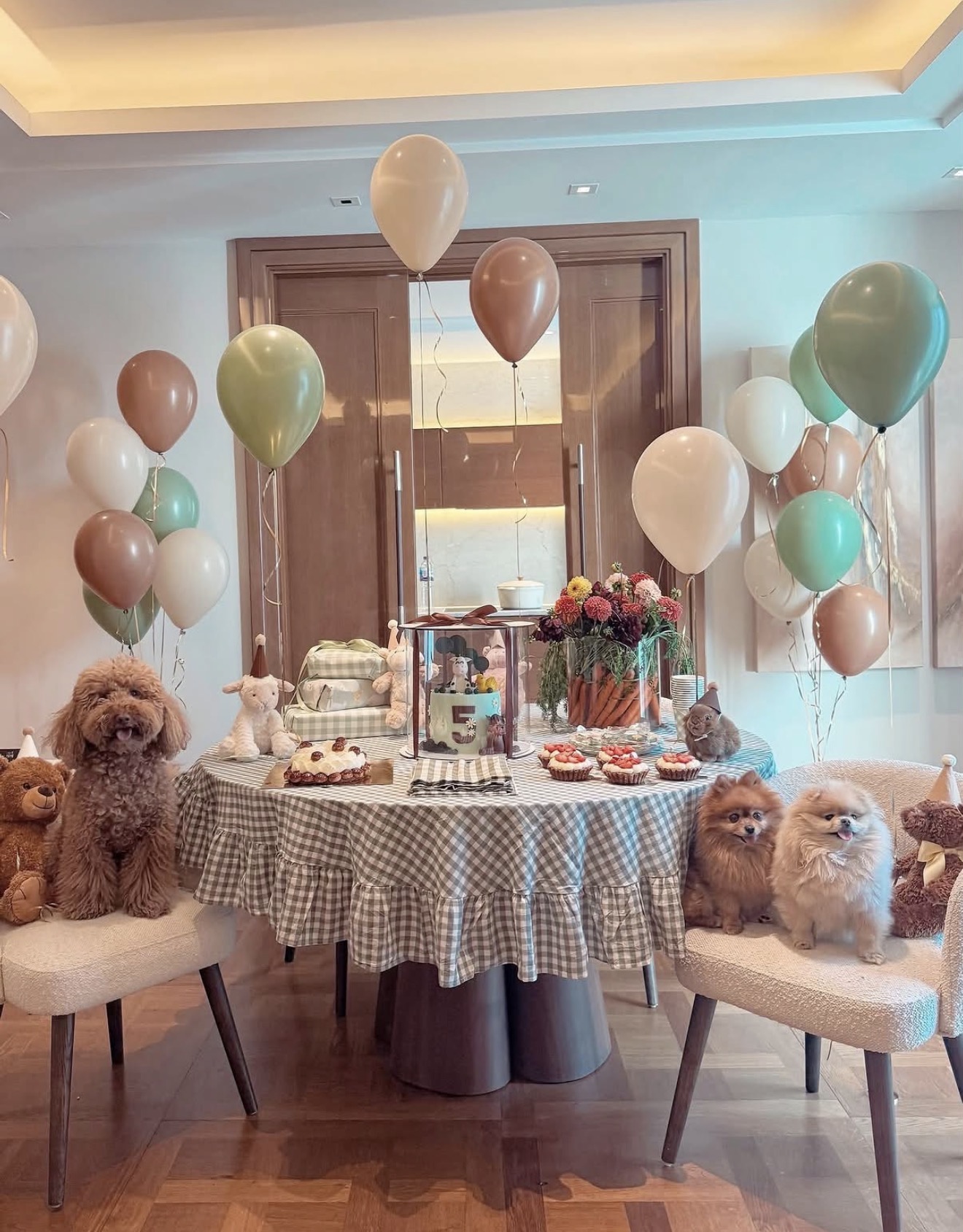 Three dogs seated at a birthday table with a cake, party hats, wrapped treats and balloons in sage and cream